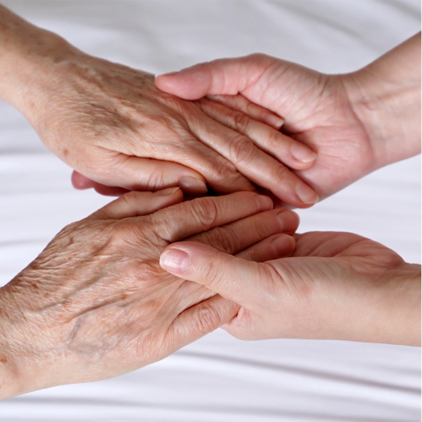 A pair of white hands gently and comfortingly clasps another pair of white hands, above a white background.